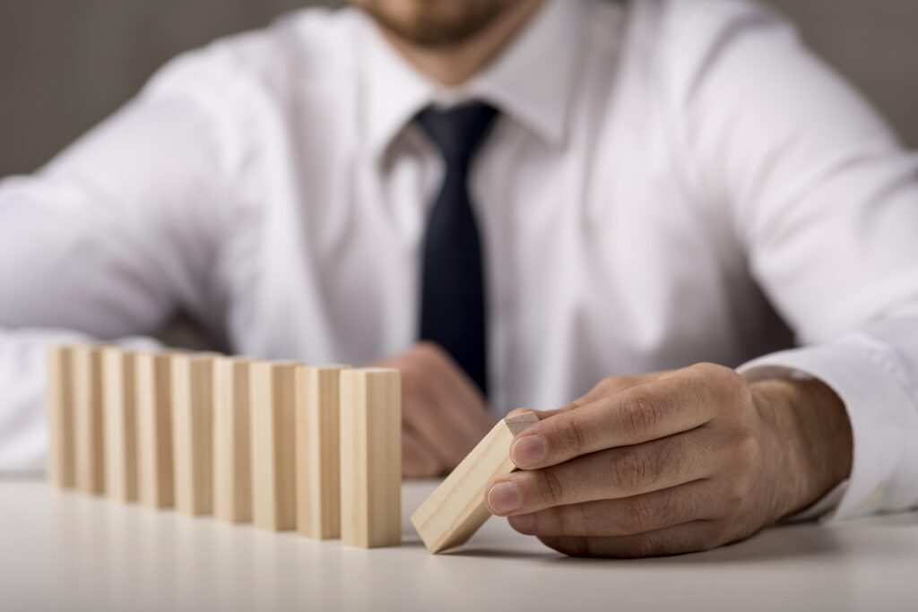 ponto de equilíbrio operacional: descubra quanto sua empresa precisa faturar para sair do zero 1 empresário desfocado de terno e gravata observando peças de dominó, representando os riscos financeiros de não conhecer o ponto de equilíbrio operacional.