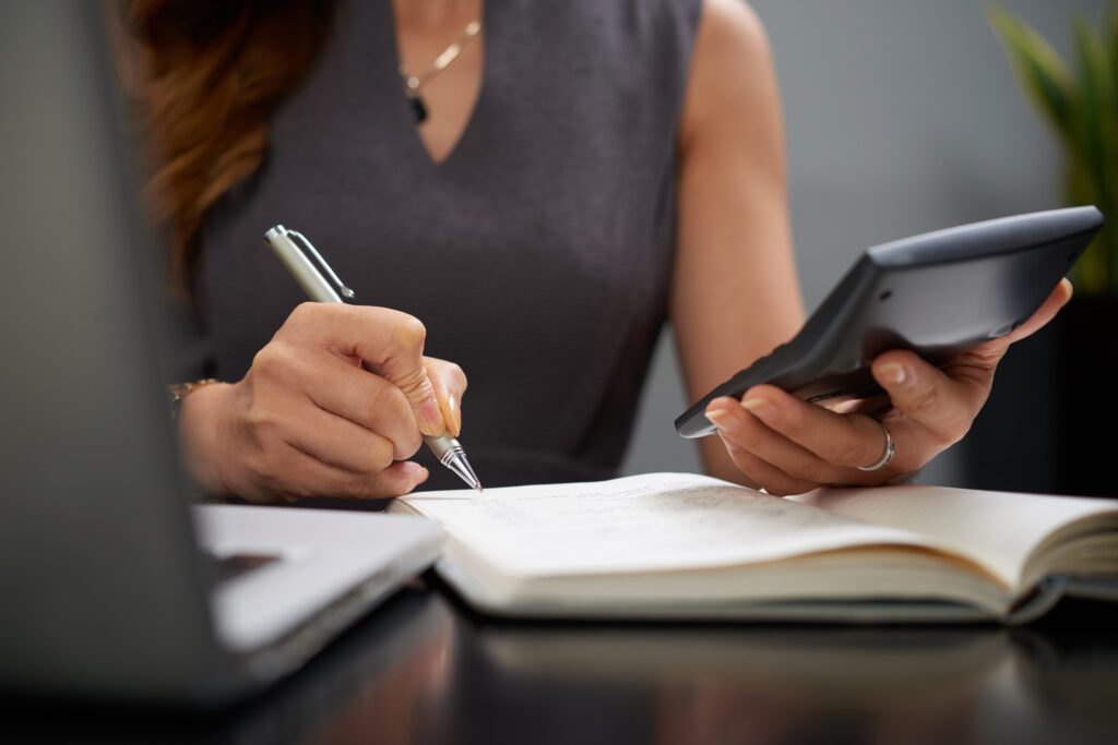 reconciliação bancária: passos para evitar erros e garantir precisão nas finanças 2 mulher segurando uma caneta e uma calculadora sobre a mesa, realizando anotações e conferência de números, representando o processo de reconciliação bancária.